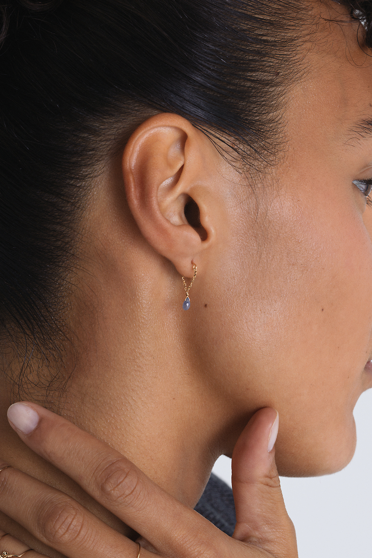 Boucle d'oreille chaîne Mia saphir bleu foncé portée, main posée sur le cou